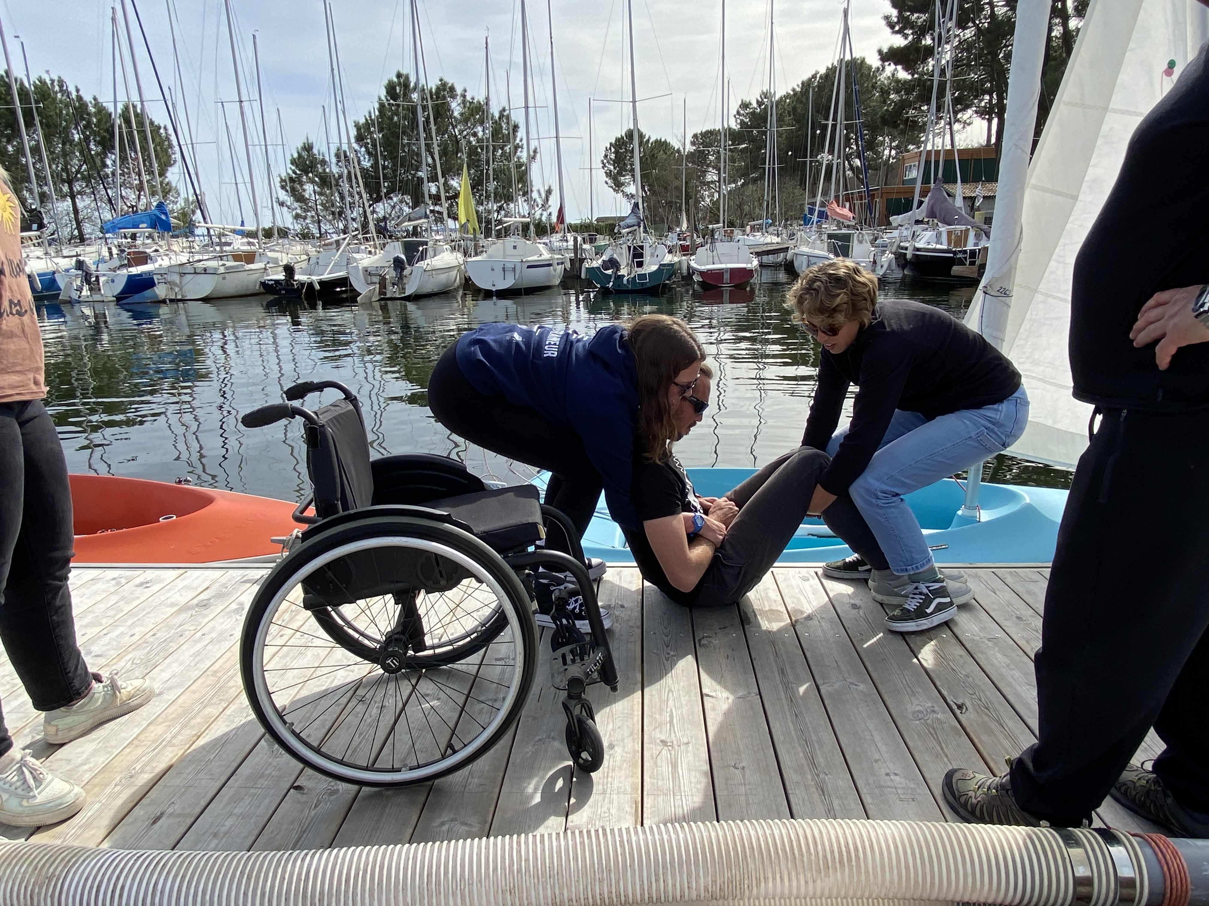 deux monitrices portent une personne à mobilité réduite pour la replacer dans son fauteuil après avoir navigué